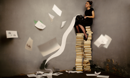 An illustration of a writer sitting on top of a stack of books.
